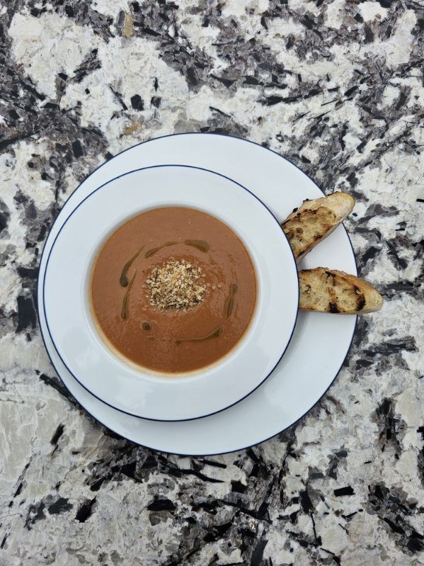 Image depicts a bowl of tomato basil gazpacho served with two slices of baguette