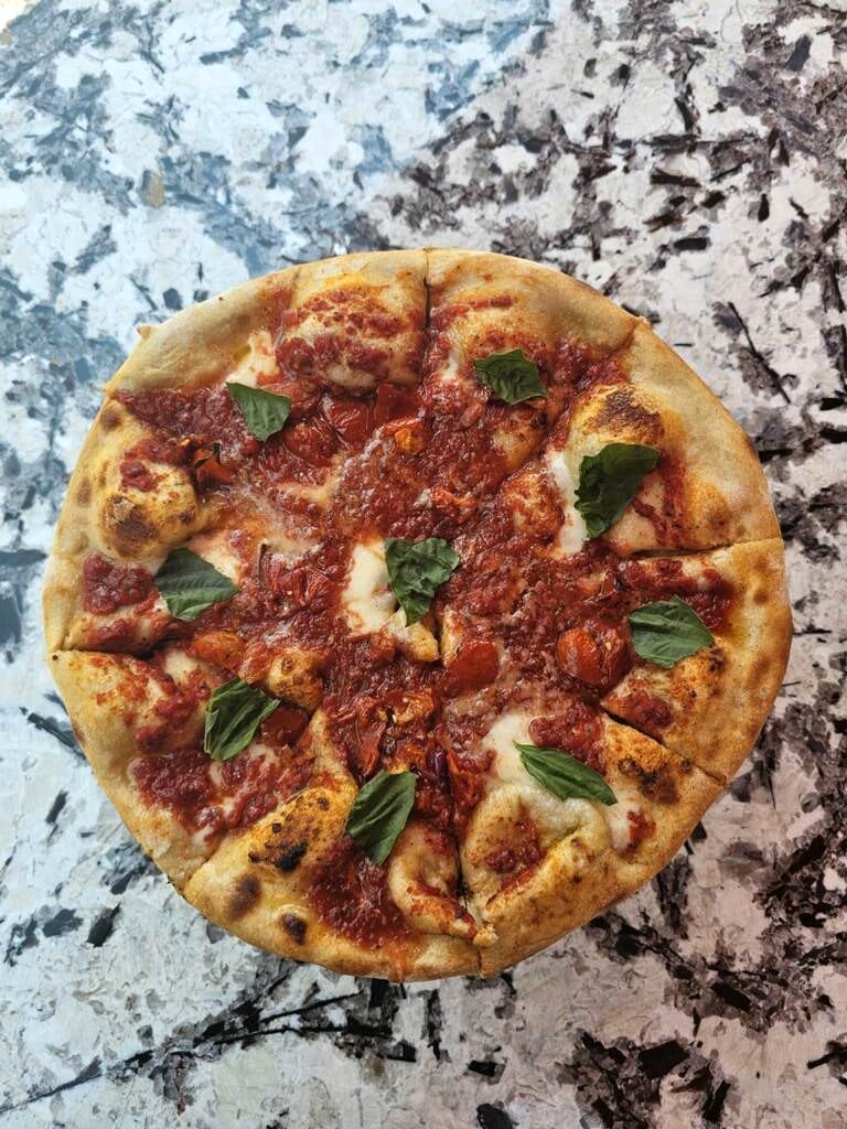 Image depicting a pizza topped with marinara sauce and fresh basil