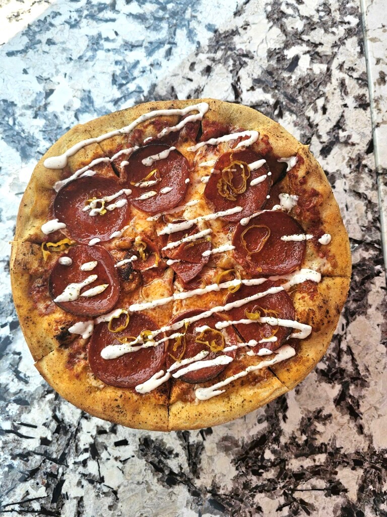 Image depicting a pizza topped with pepperoni and drizzle of ranch